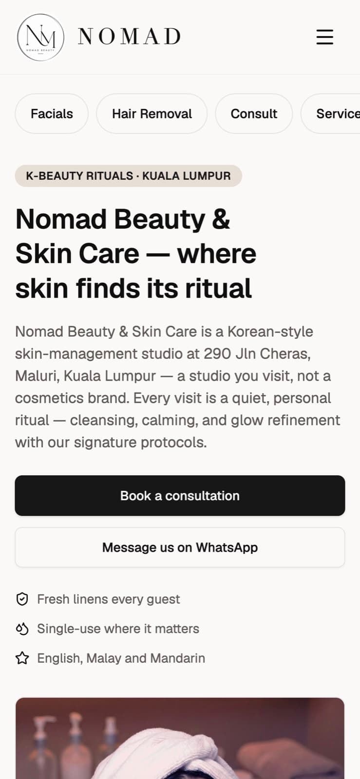 NOMAD Beauty & Skin Care home page on a phone, showing the Book a consultation and Message us on WhatsApp buttons.